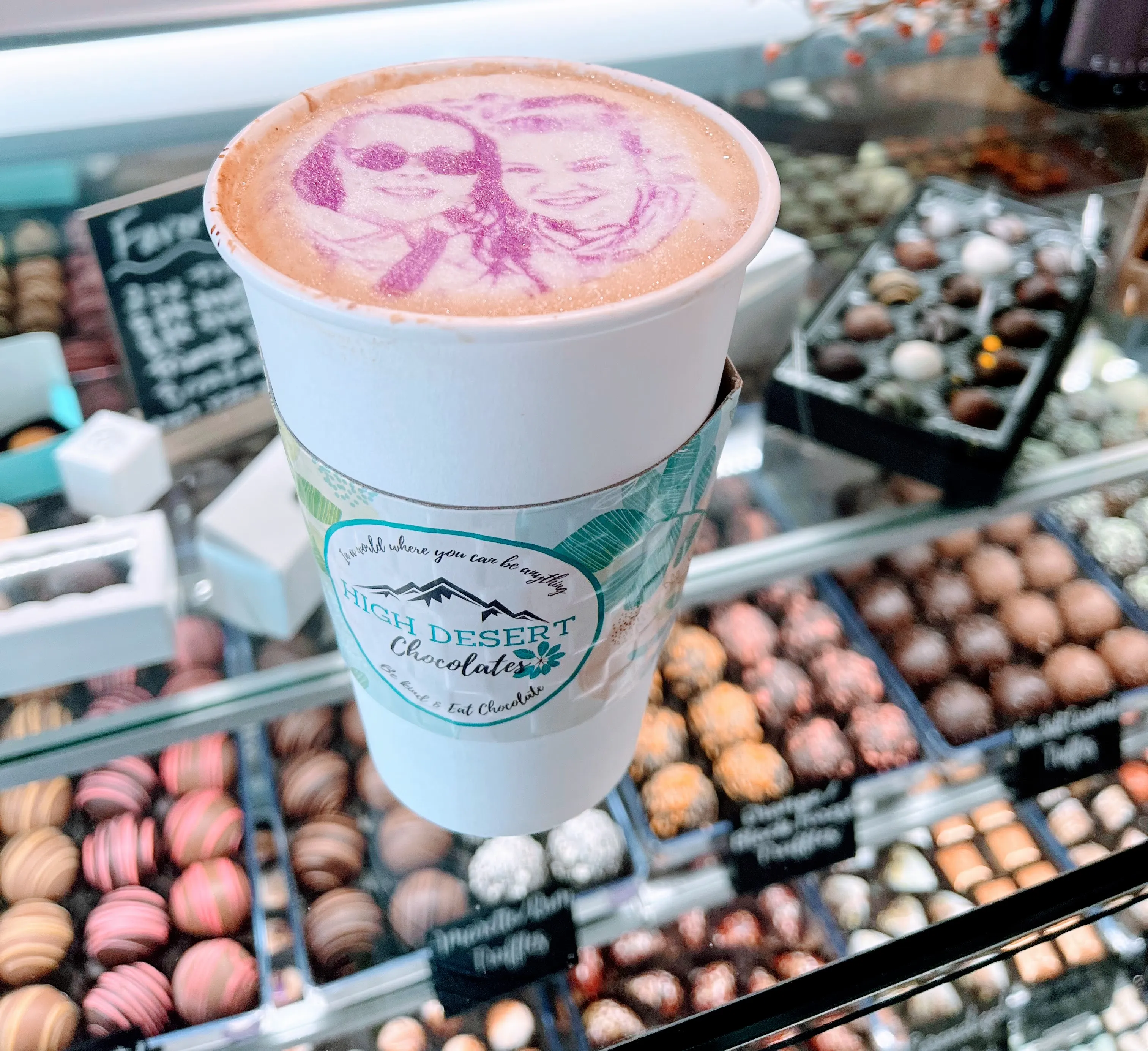 A printed-art latte beside a glass display case of artisan truffles at High Desert Chocolates