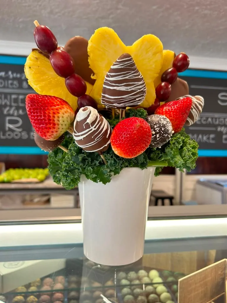 A fruit arrangement of chocolate-dipped strawberries, pineapple, and grapes in a white vase at High Desert Chocolates