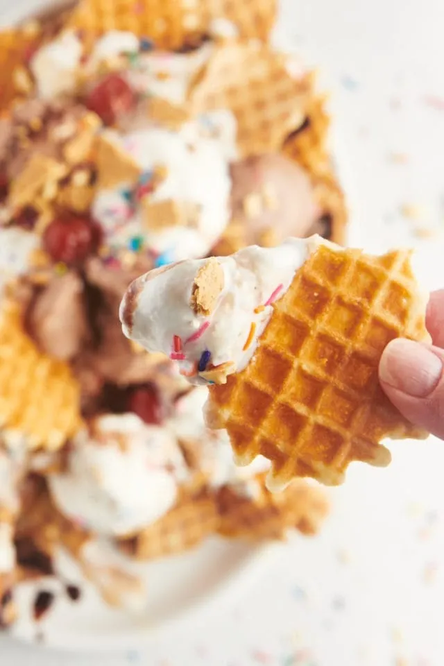 A waffle chip scooping up ice cream nachos loaded with sprinkles and cherries