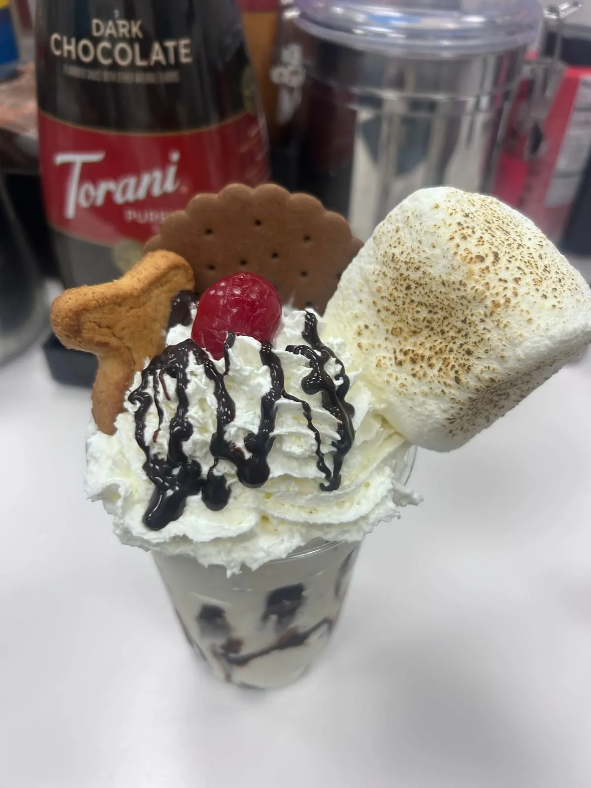 A tall s'mores milkshake topped with whipped cream and a toasted marshmallow